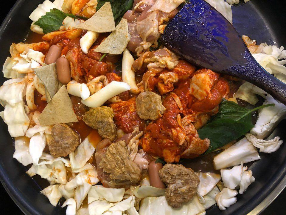 Dakgalbi being cooked in a pan, showcasing a mix of spicy marinated chicken, fish cakes, sausages, and vegetables for a flavorful Korean dish.